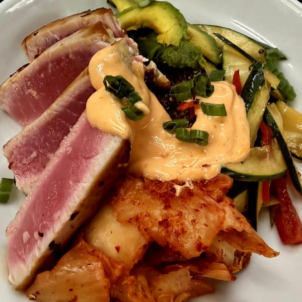 Seared tuna slices with avocado, kimchi, and a creamy orange sauce, garnished with green onions.