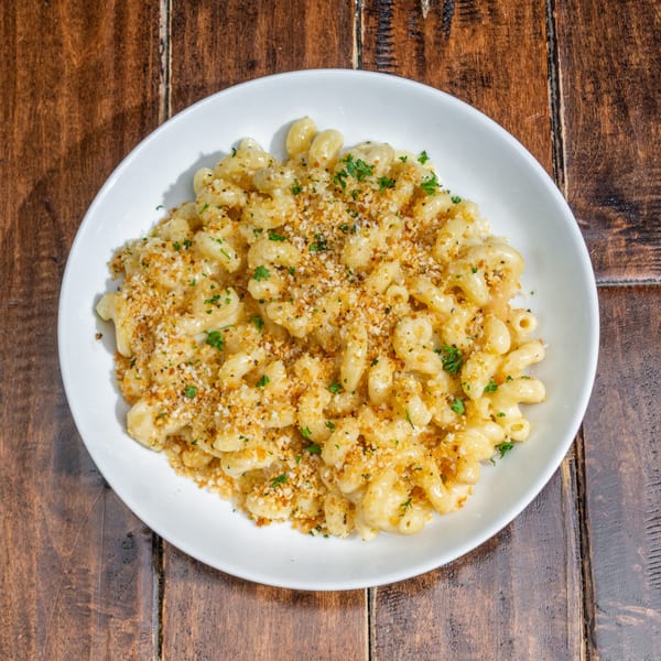 Creamy macaroni and cheese topped with golden breadcrumbs and fresh parsley in a white bowl.