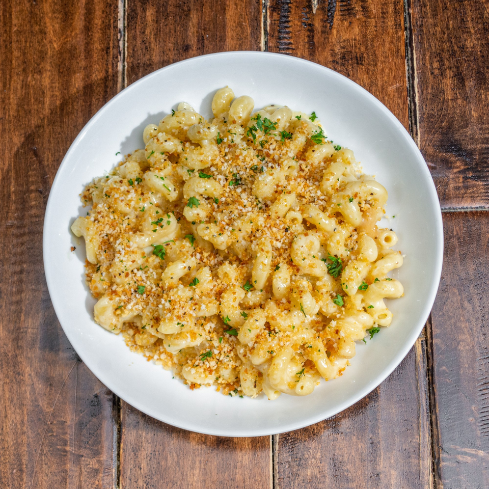 Creamy macaroni and cheese topped with golden breadcrumbs and fresh parsley in a white bowl.