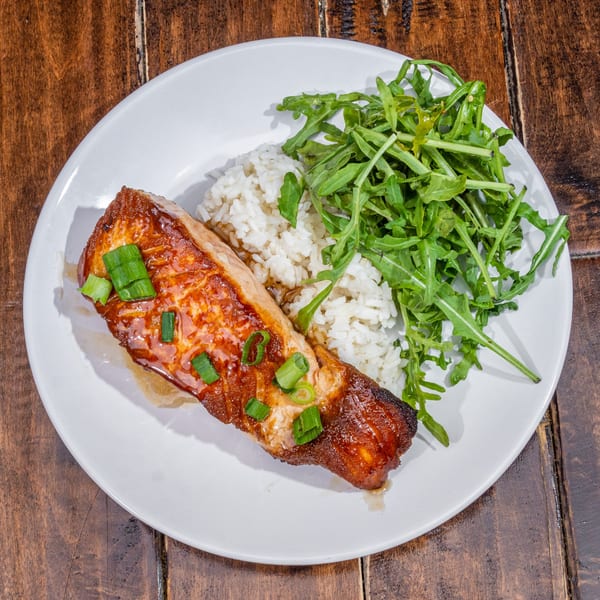 Glazed salmon with chopped scallions, white rice, and a side of fresh arugula on a white plate.