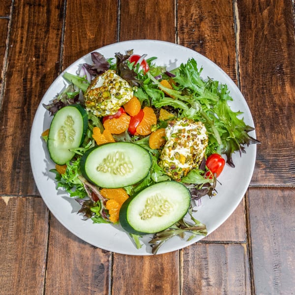 A fresh salad with mixed greens, cucumber, mandarin oranges, cherry tomatoes, and pistachio-crusted goat cheese.