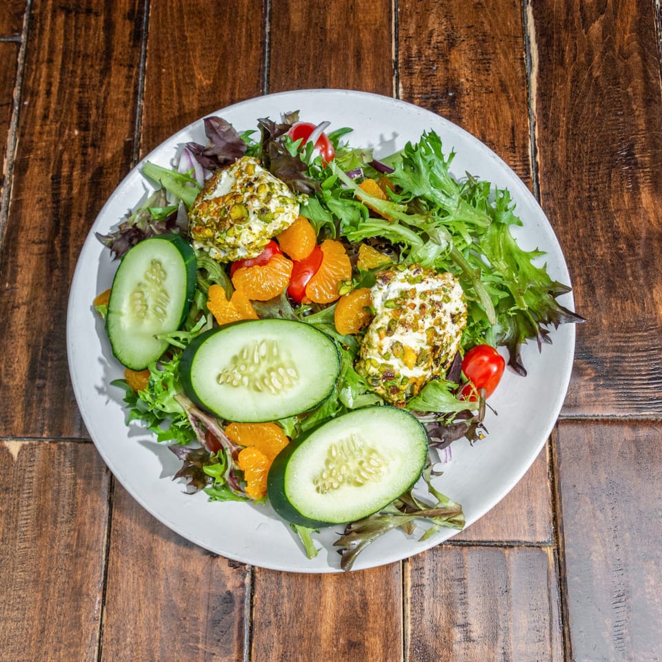A fresh salad with mixed greens, cucumber, mandarin oranges, cherry tomatoes, and pistachio-crusted goat cheese.