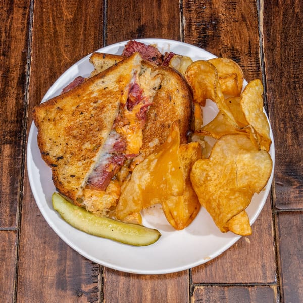 Grilled sandwich with melted cheese, corned beef, sauerkraut, chips, and a pickle spear.