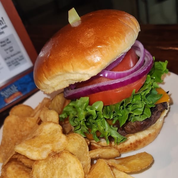 A cheeseburger with lettuce, tomato, and red onion, served with a side of potato chips.