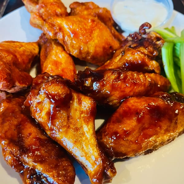 A plate of glistening, saucy chicken wings with a side of celery sticks and ranch dressing.