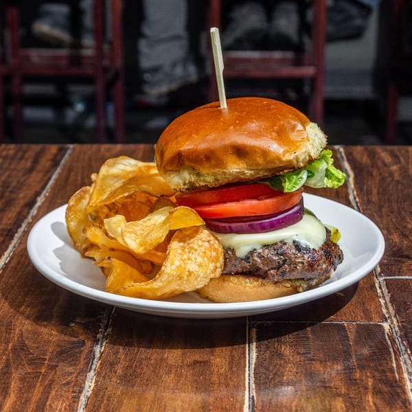 A cheeseburger with lettuce, tomato, and onion, served with crispy potato chips on a white plate.